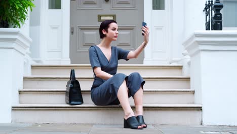 mujer elegante sentada en los escalones de un edificio tomando selfies