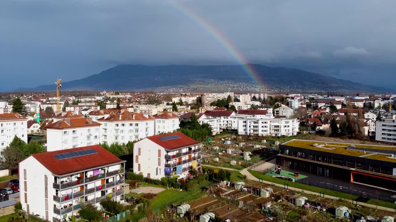 toma de drones de una zona residencial recientemente construida y jardines comunales con un arco iris y nubes oscuras en el fondo