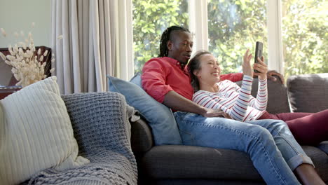 happy diverse couple relaxing on couch using tablet in living room, copy space, slow motion