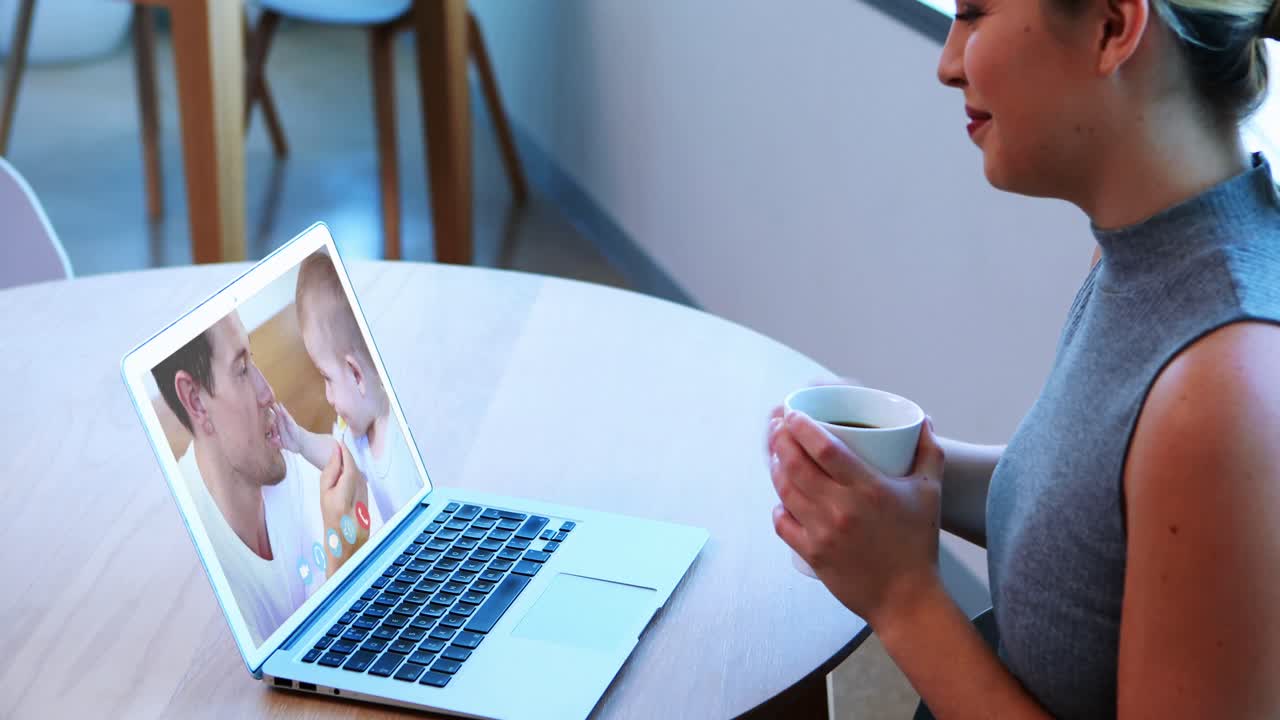 クリエイティブなビジネスウーマンがコーヒーカップを持ちながら、ノートパソコンでビデオ通話をしている。