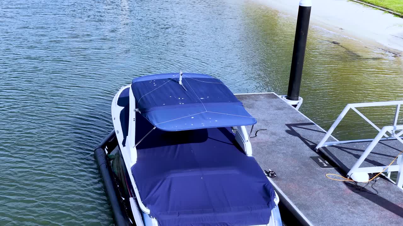 Drone slowly pulls back from a moored boat at marina, revealing waterway and coastal landscape