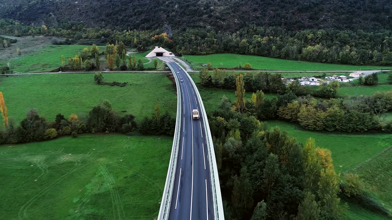 una vista aérea panorámica sobre las carreteras que entran en un túnel en francia. sólo campos de hierba y árboles alrededor de las carreteras. coches y camiones conduciendo en las calles.