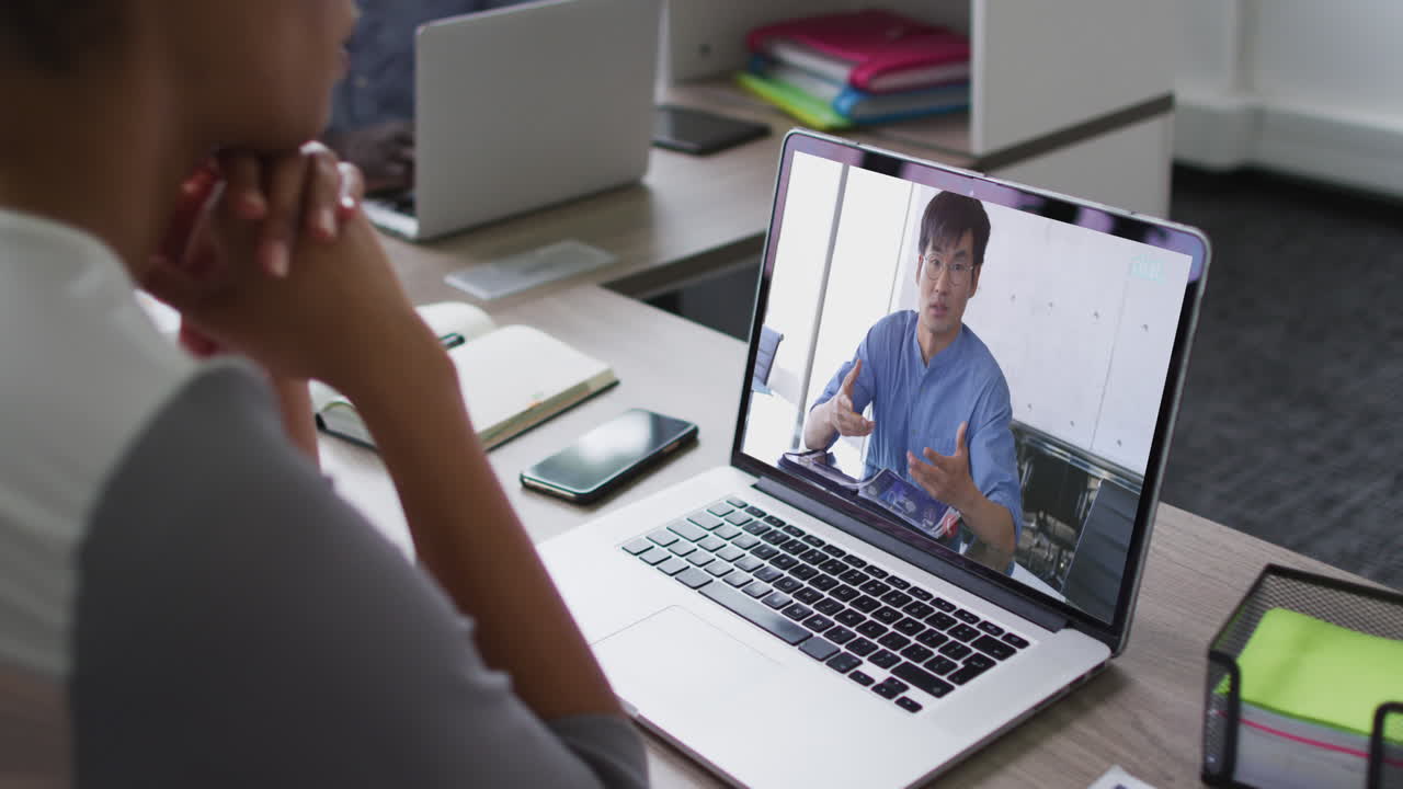 mujer de negocios afroamericana sentada en un escritorio usando una computadora portátil haciendo una videollamada con un colega masculino