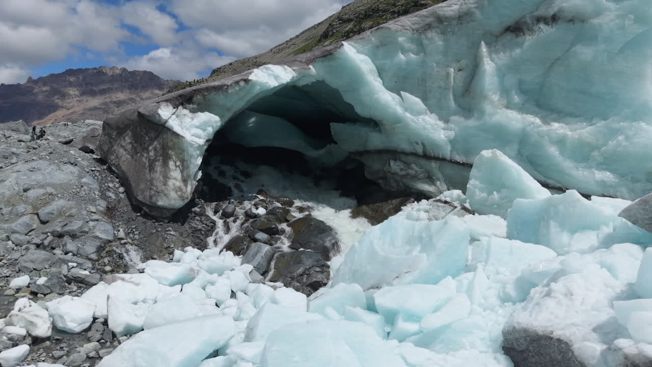 Drone pans right to left over icy cave, flowing water, and rocky terrain