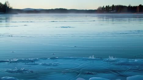 this captivating winter landscape showcases a frozen lake during dusk, with the sun setting in the background. mist rises gently from the icy surface, enhancing the tranquil atmosphere.
