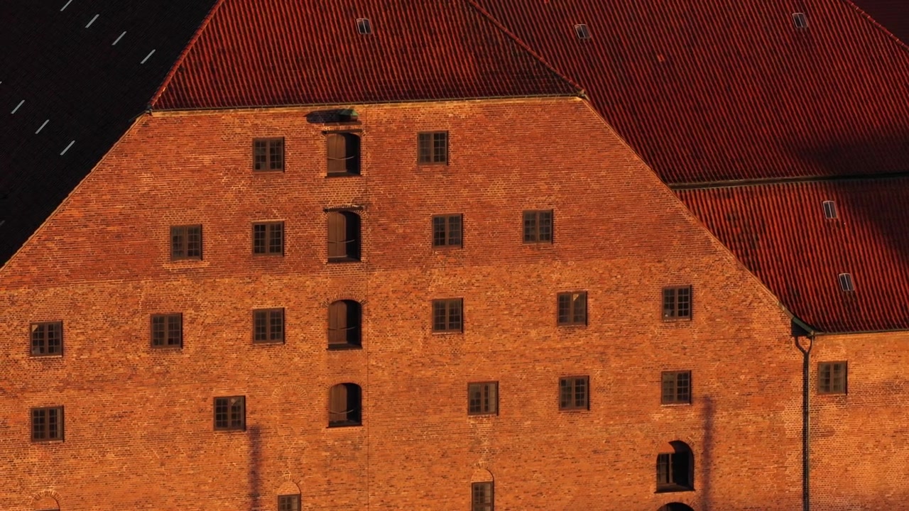 Vista aérea de drone de um armazém histórico de tijolos vermelhos com um telhado íngreme de telhas sob uma luz dourada quente, Copenhague, Dinamarca