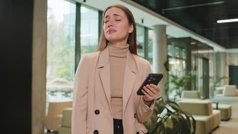 young businesswoman using smartphone becomes shocked sudden lottery results in office hotel lobby