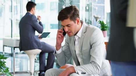 Businessman-picking-up-a-call-while-working-in-laptop