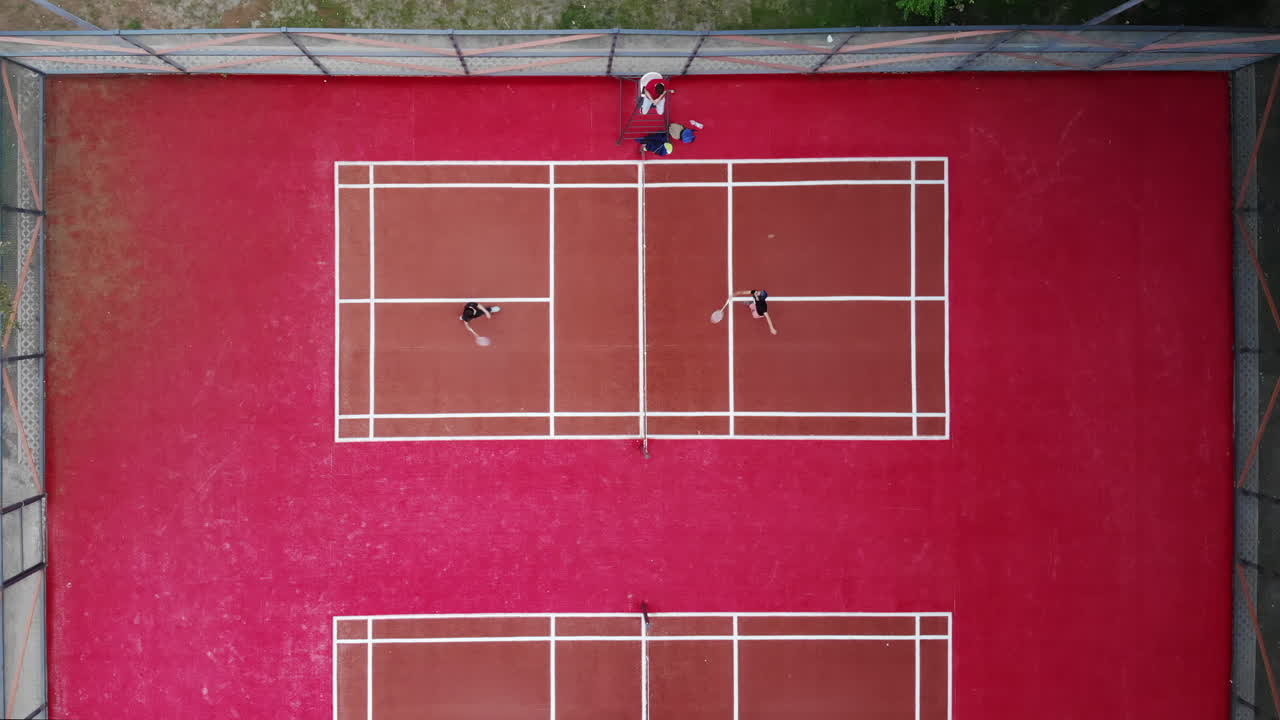Two pairs of players engage in an intense tennis match on striking red courts at a park in the afternoon. The excitement and skill are evident in every rally