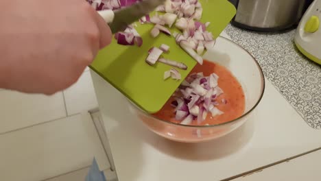 mujer caucásica cocinando y poniendo cebolla morada cortada en salsa casera