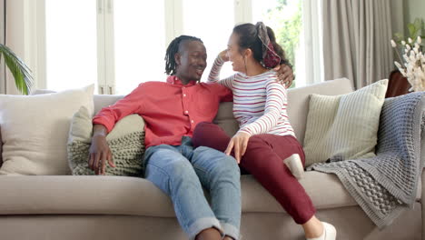 Portrait-of-happy-diverse-couple-sitting-on-couch-talking-in-sunny-living-room,-slow-motion