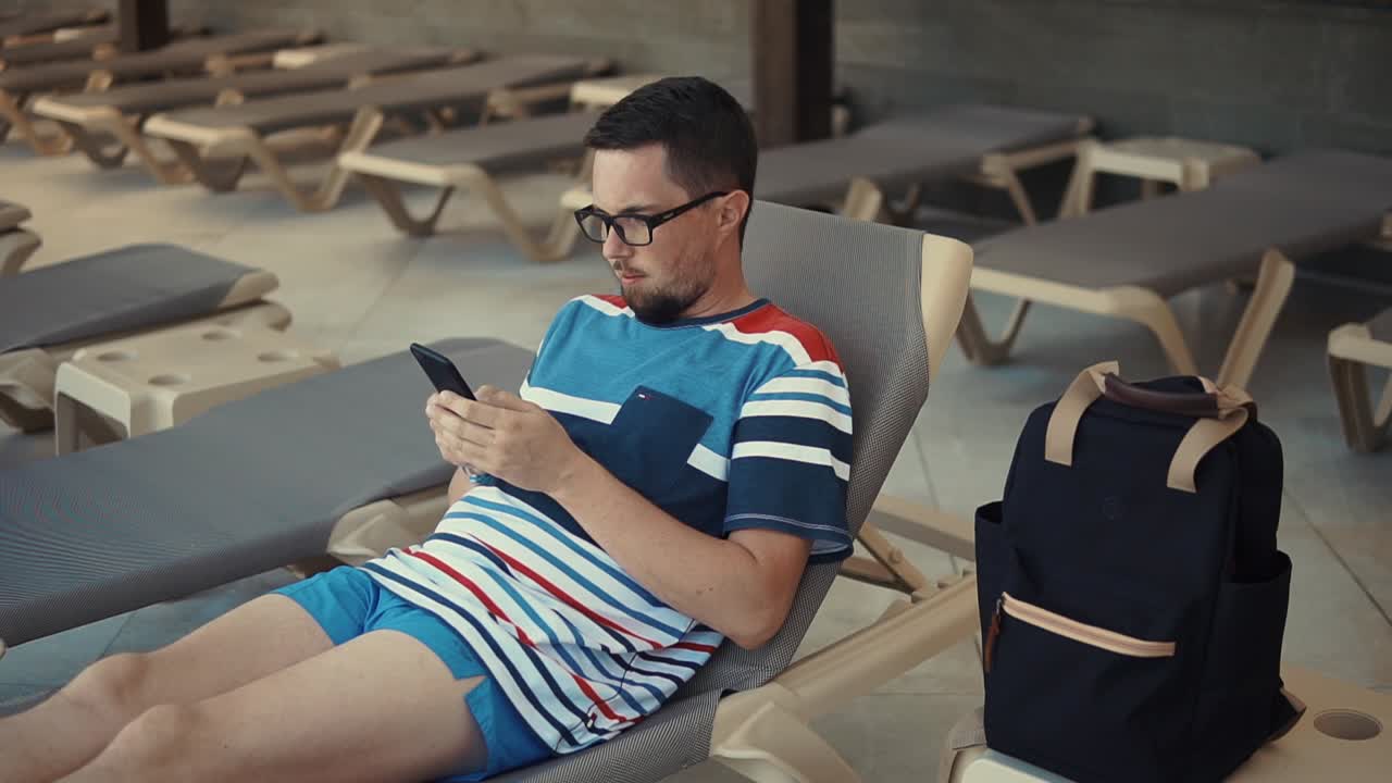 hombre relajándose junto a la piscina usando su teléfono