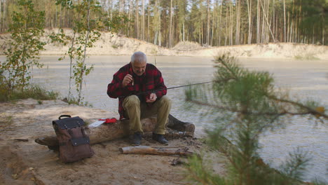 pesca en la orilla de un lago limpio en el bosque pescador está eligiendo cebo y poniéndolo en el gancho de la vara tiempo de relajación