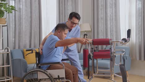 side view of asian male nurse helping patient in wheelchair using walker to stand by himself during a physical therapy at home