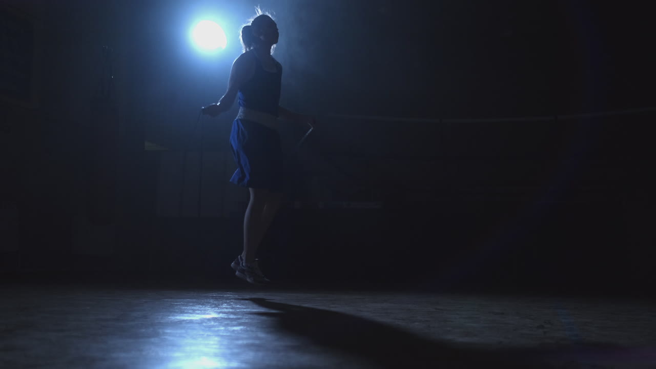 체육관에서 훈련하는 아름다운 젊은 여성 권투 선수가 로프를 뛰어넘어 카메라 슬라이드의 움직임을 보여줍니다.