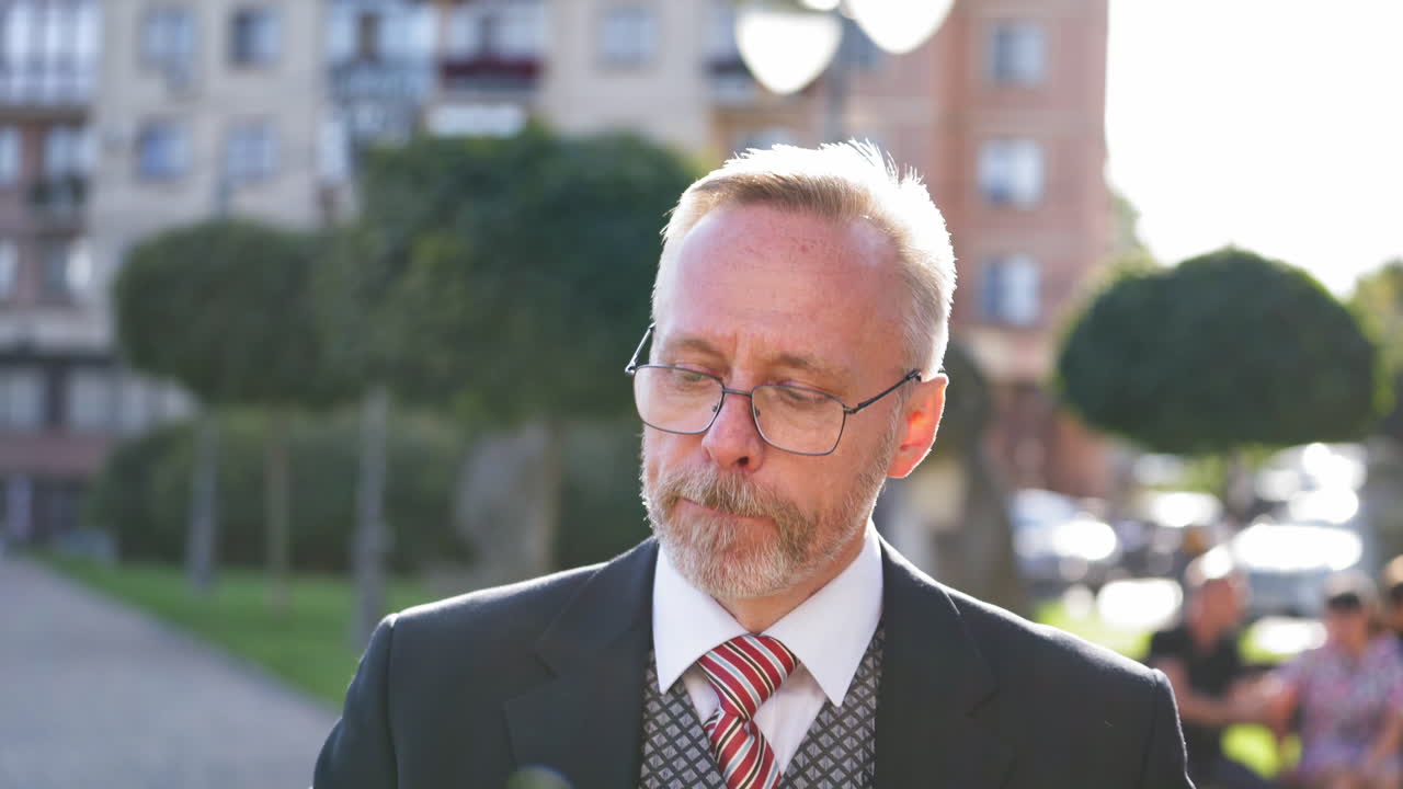 Thoughtful mature man smoke outdoors. Nervous middle aged businessman in glasses smoking cigarette standing on the city background.