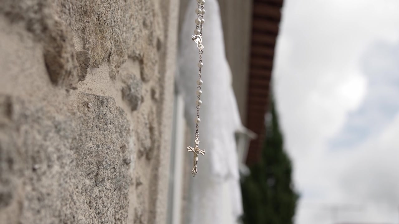 Close up of rosary crucifix hanging against textured stone wall in soft light
