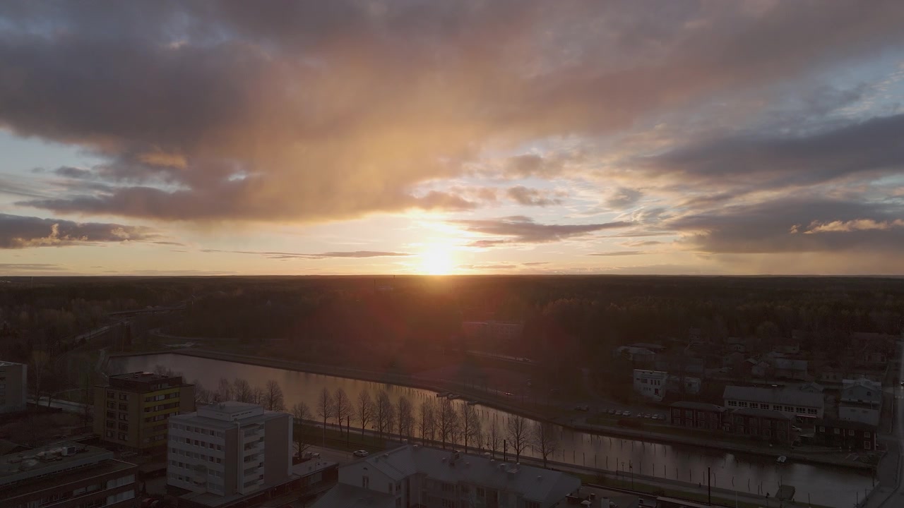 Tomada de drone lenta com movimento lateral de prédios de apartamentos, árvores, rio e o pôr do sol. Filmado em Uusikaupunki, Finlândia.