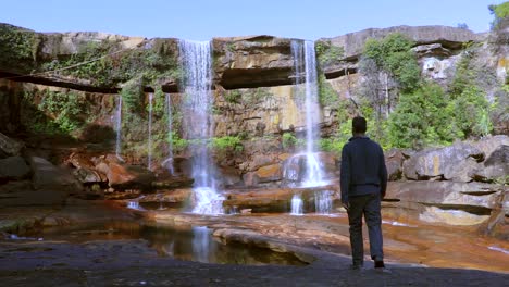 joven disfrutando de la prístina cascada natural que cae desde la cima de la montaña en el día desde un video de ángulo bajo tomado en phe phe fall meghalaya india