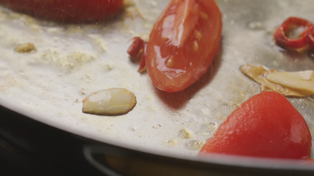 Close-Up of Frying Tomatoes, Garlic and Red Chili Slices in Steel Pan