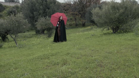 woman walks with red umbrella on a meadow on a gloomy rainy day