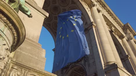 european union flag waving under historic stone monument