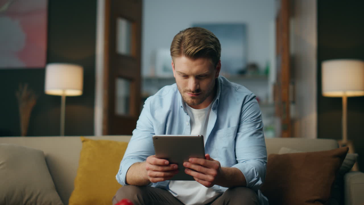 Serious guy working tablet at home. Focused freelancer holding pad sitting sofa