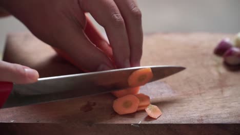 close-up of hands slicing a fresh carrot on a wooden cutting board. the scene highlights the preparation process in a natural kitchen setting with soft lighting