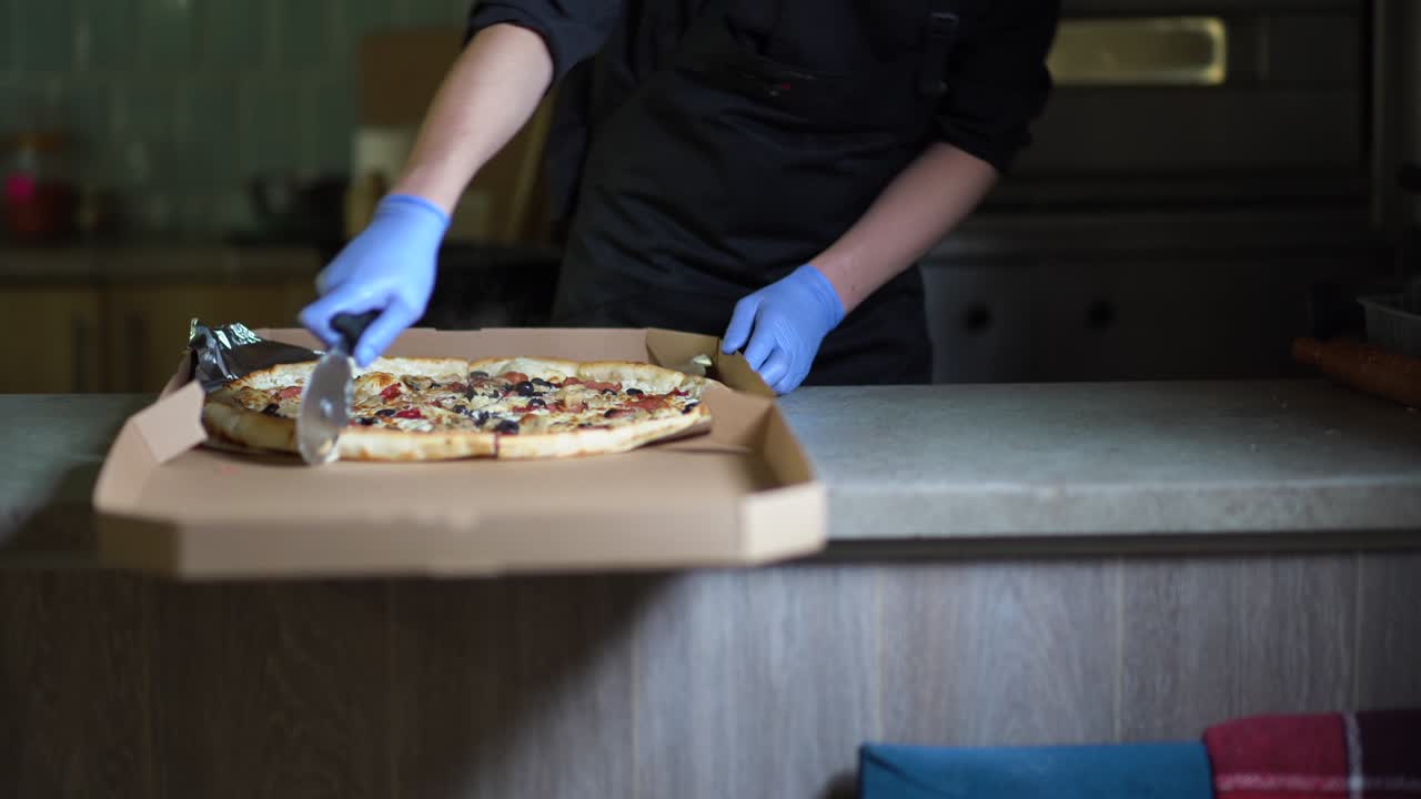 lo chef maschio taglia la pizza finita con un coltello circolare. scatola di pizza, cibo da asporto durante una pandemia.
