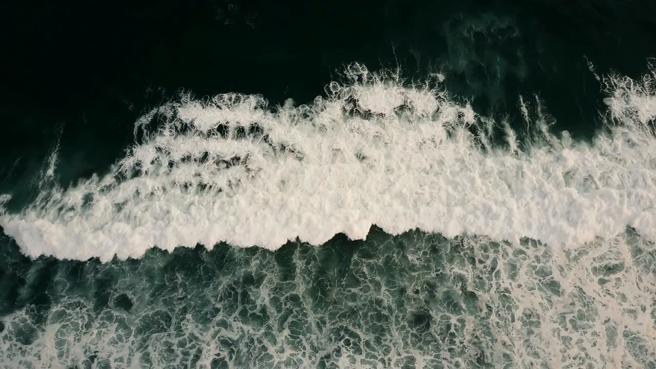 Drone moving right over huge wild dark blue open ocean waves crashing down, white seafoam creating epic natural texture