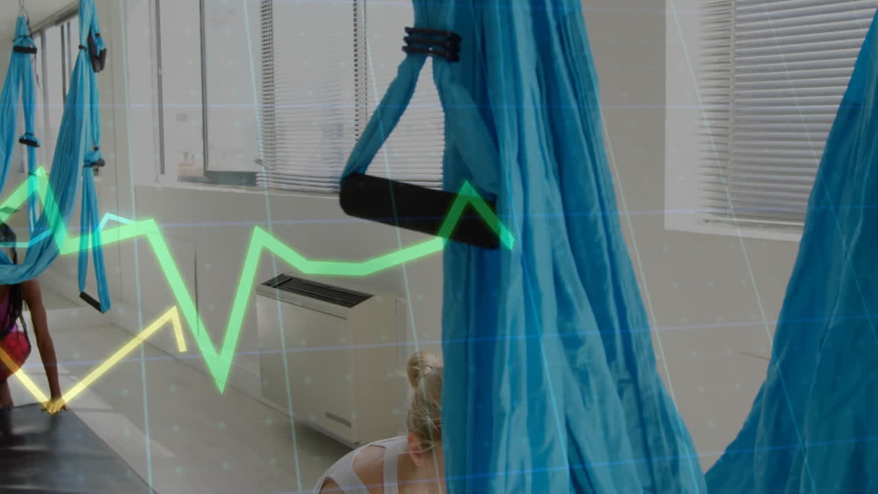 Practicing aerial yoga, people in class with green financial graph animation overlay