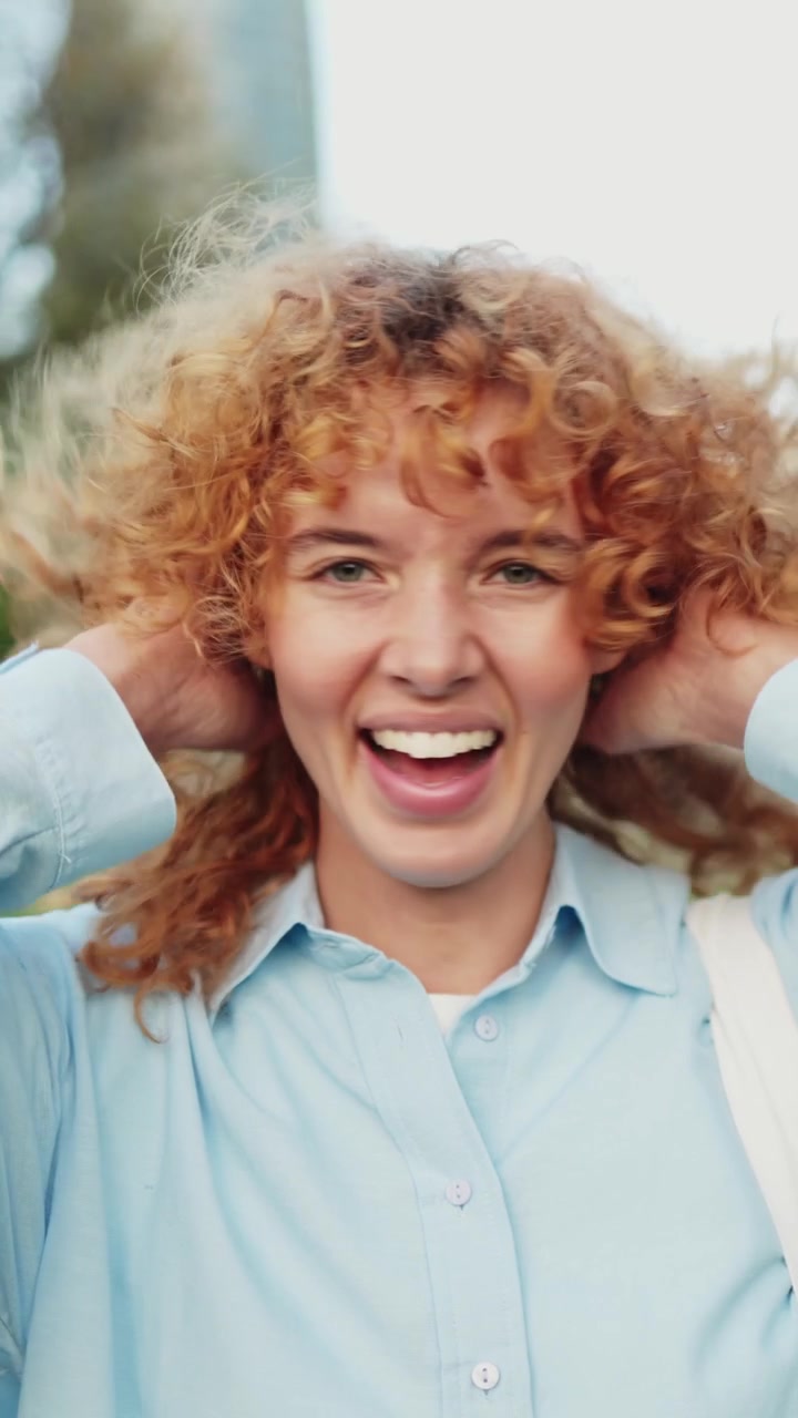 Giovane donna felice con capelli rossi ricci che sorride e ride in un parco.