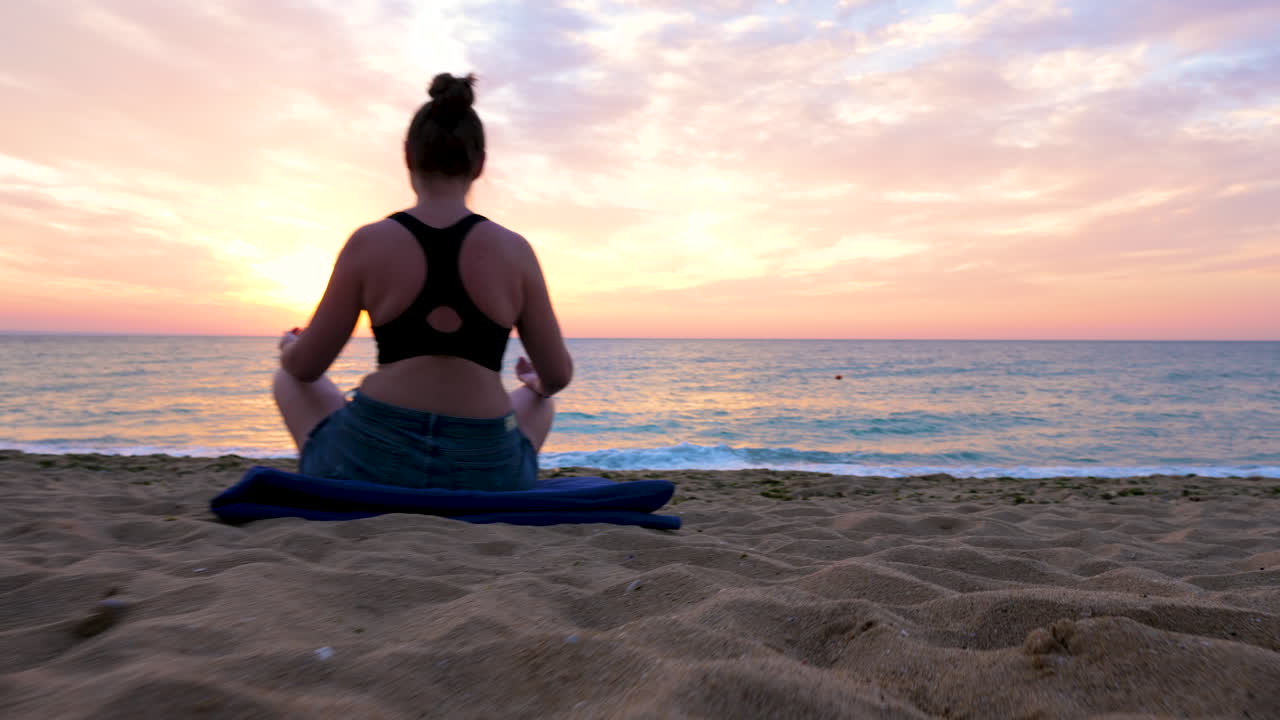 Woman sits on the beach practicing yoga at the sunrise