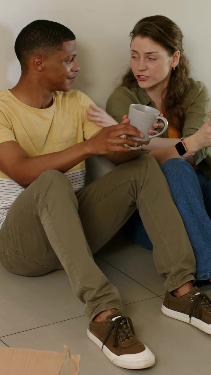 Vertical video: Reaching man and woman passing gray mug on tiles at home during move, smartwatch