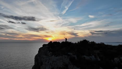 cinematic reveal of person standing on ocean cliff edge at sunset in spain