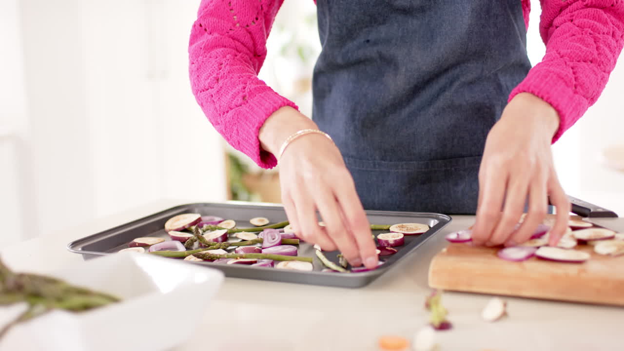 sección media de una mujer biracial preparando comida en la cocina en casa con espacio de copia, cámara lenta