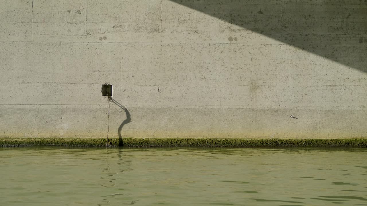 Concrete wall and water with shadow, small pipe hanging down