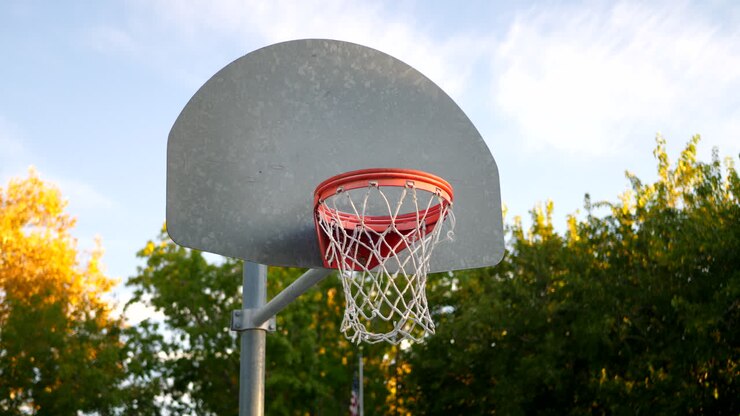 tiro deslizante a la izquierda de un aro de baloncesto con un tablero de metal, borde naranja y red en una cancha de parque vacía al amanecer