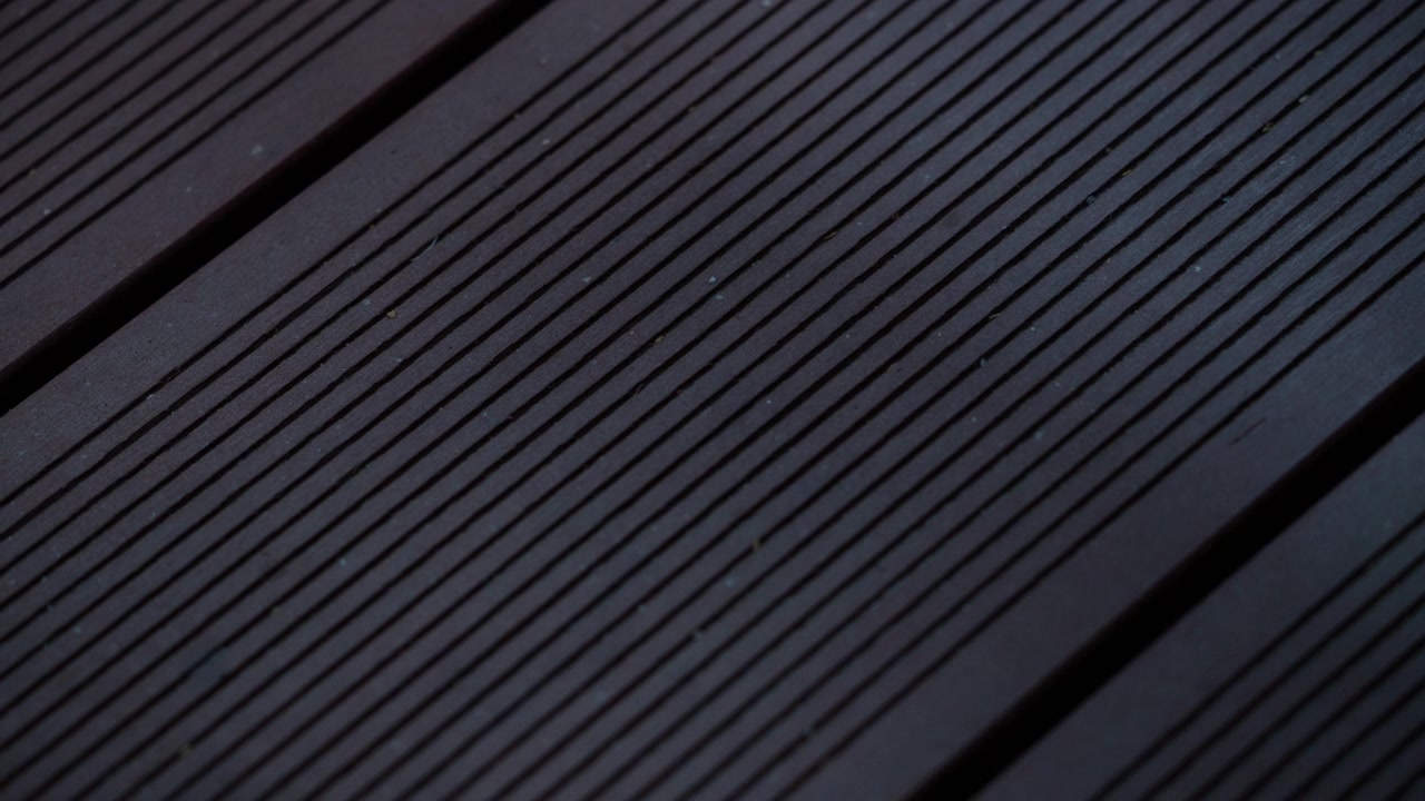 Detailní filmový záběr tmavých dřevěných terasových prken s lineárními drážkami a geometrickými vzory.