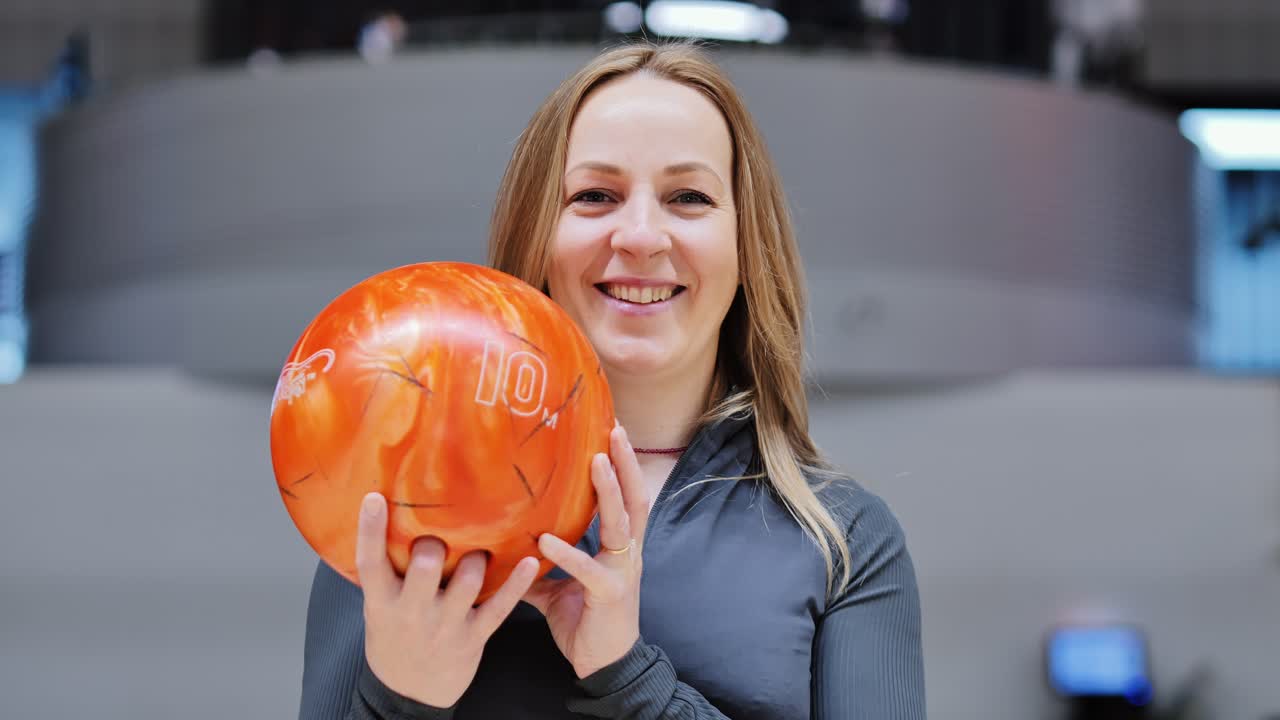Smiling woman focusing before throw with orange ball in bright alley, close shot