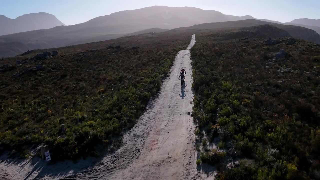 Cyclists race down a gravel road and through a gate on a mountain trail