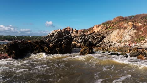 drone orbits around eroded sheets of rocks sticking out from ocean as waves churn the water below