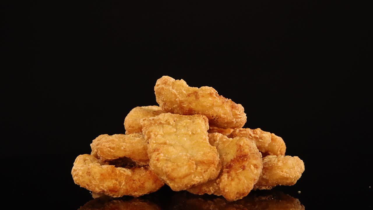 A pile of crispy chicken nuggets spins smoothly on a glossy black surface, illuminated by soft studio lighting, highlighting texture and appetizing color