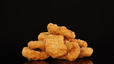 a pile of crispy chicken nuggets spins smoothly on a glossy black surface, illuminated by soft studio lighting, highlighting texture and appetizing color