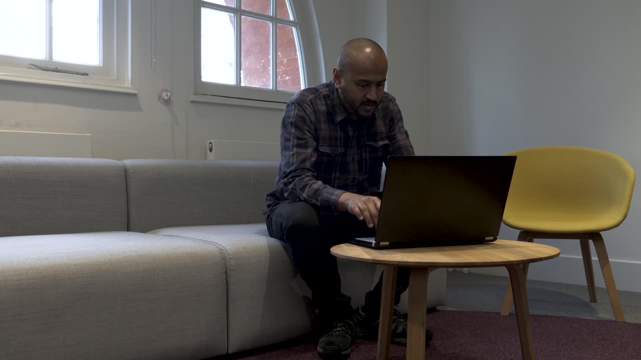A static shot of a businessman sitting on a couch working on his laptop
