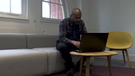 una toma estática de un hombre de negocios sentado en un sofá trabajando en su computadora portátil