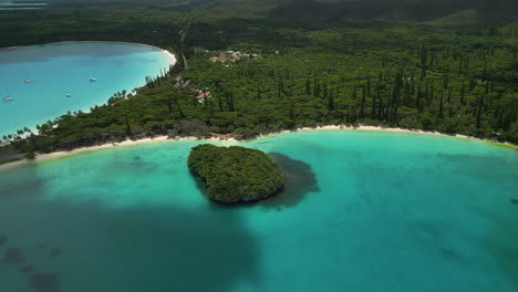 La-Bahía-De-Kanumera,-El-Agua-Cristalina-De-La-Isla-De-Los-Pinos,-La-Playa-Prístina-Y-El-Islote-De-Roca-Sagrada:-Revelación-De-Retroceso-Aéreo