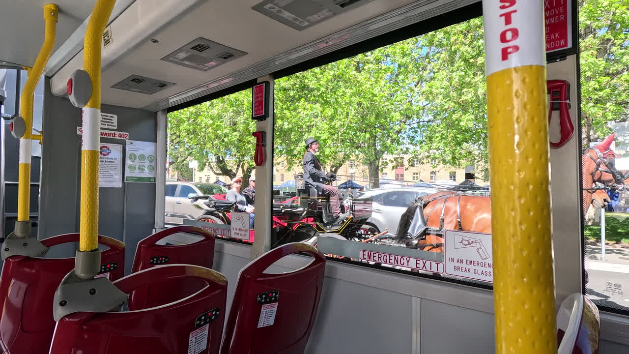 Sitting on a bus, a horse and cart leisurely trot by, creating a serene moment in a peaceful town. The bright day enhances this charming sight.