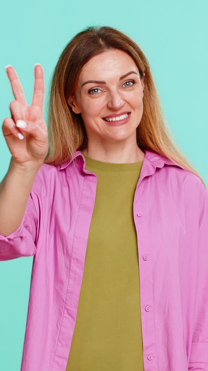 Woman showing peace sign with two fingers and smiling expressing positivity harmony and friendliness