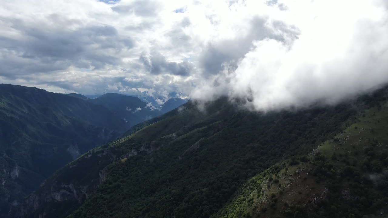 Landscape view of mountains and cloudy sky The scene is lush with trees Clouds cover the tops of the mountains in the distance